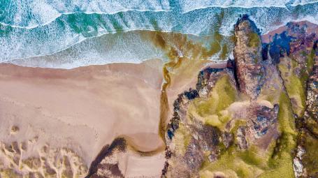 An aerial photograph of a sea shore with sand and rocks 